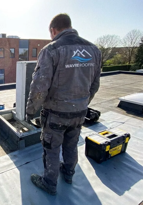 Étancheur de Wavre Roofing debout sur un toit plat à Wavre, près d'une costière de groupe extérieur en cours d'habillage